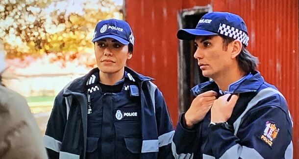 Two officers outside a red building in A Remarkable Place to Die