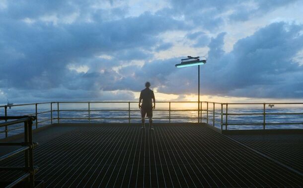 A lone figure walking a long pier toward the sunset in Digger