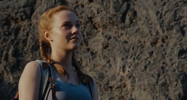 A climber on the rock face in Fall 2: Deadpoint (2026). The guide, Jon, hands Jax and Luce oxygen tanks that turn out to be full of fentanyl