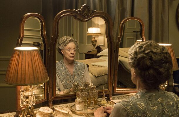 An elderly Englishwoman at her dressing-table mirror in a period drama