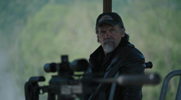 A bearded survivalist watching the horizon through a rifle scope